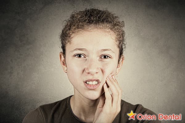Stock image of a person wincing while holding their jaw in discomfort