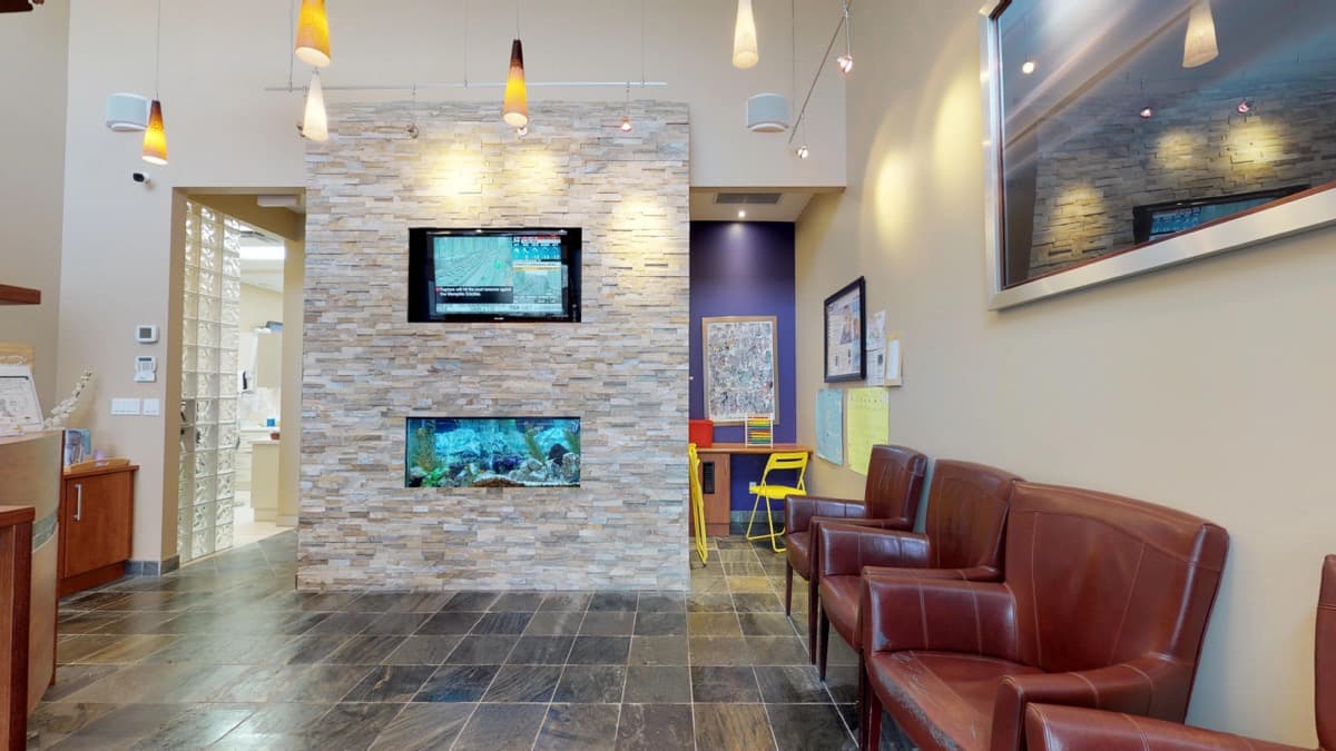 The waiting area at Orion Dental Milton, with a stone feature wall, a built-in aquarium and leather seating