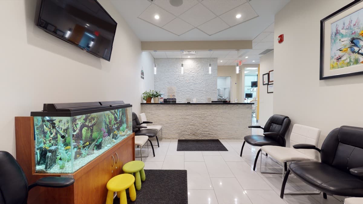 The waiting area at Orion Dental Scarborough, with an aquarium on a wood cabinet, small stools for children and a stone-clad reception desk