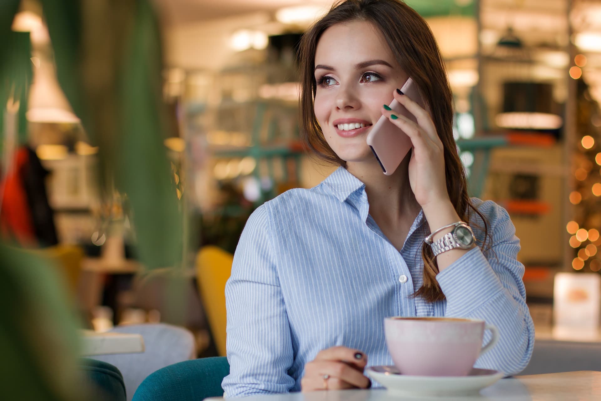 Stock image of a woman smiling while on the phone, with a cup of coffee